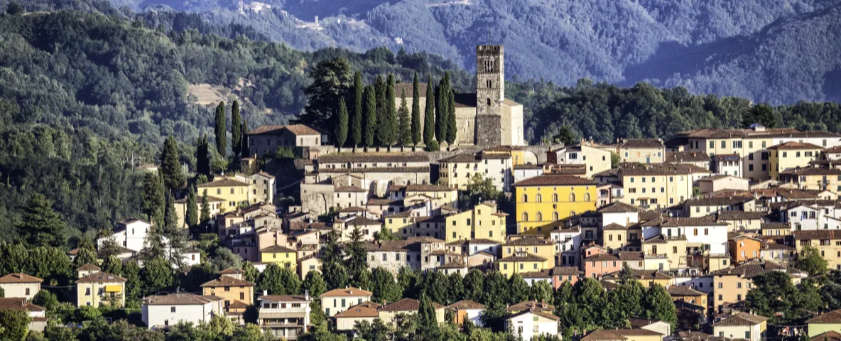 Borgo collinare con campanile, circondato da boschi e montagne